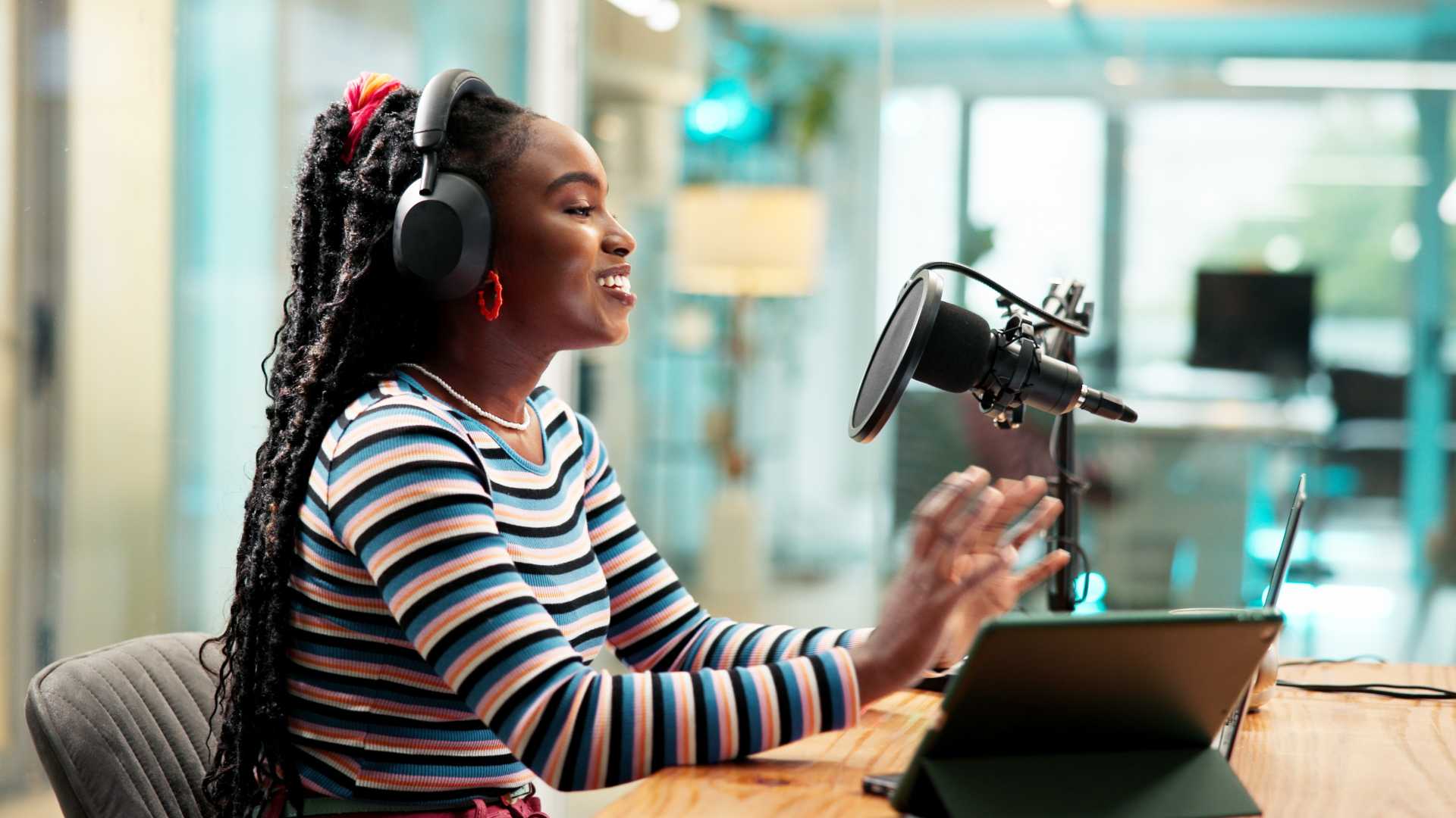 Woman wearing headphones recording a podcast with a microphone and tablet in a modern office.