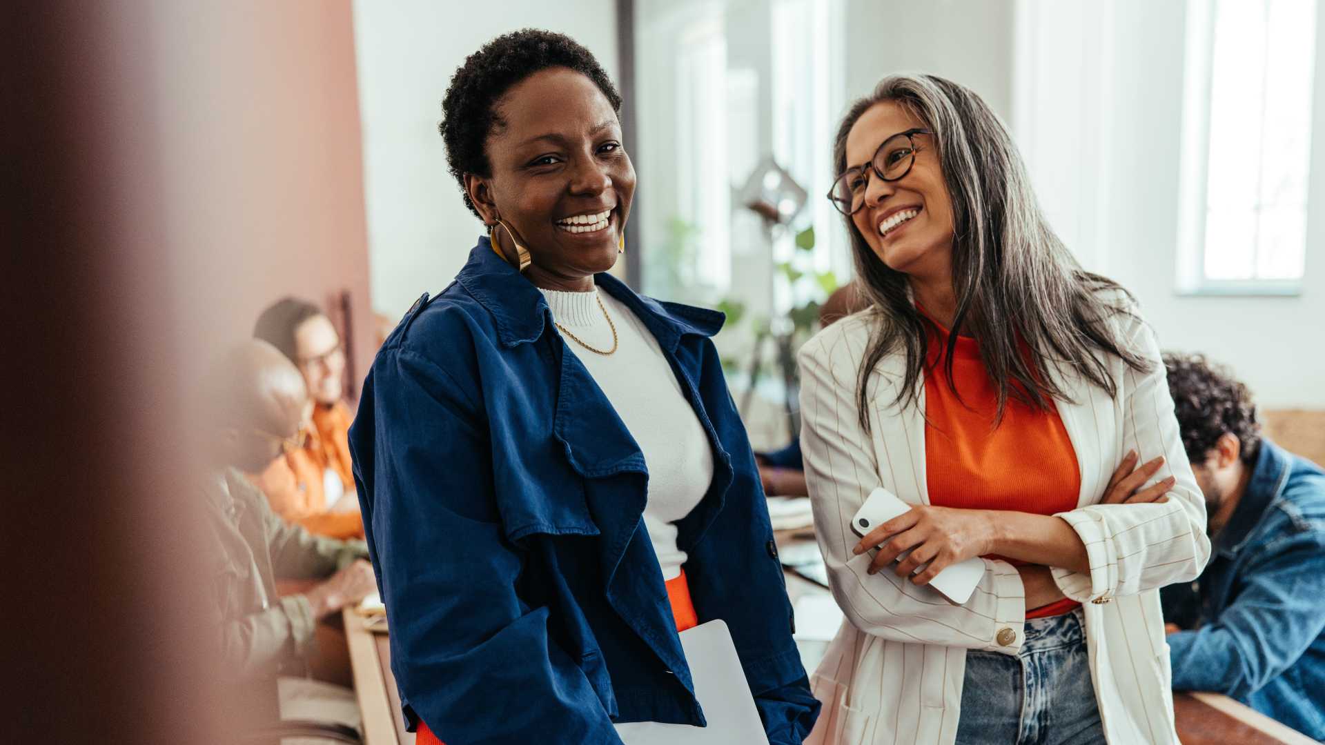 Two employees smile and chat in a collaborative office environment, illustrating the workplace relationships and social connections that support employee engagement and teamwork.