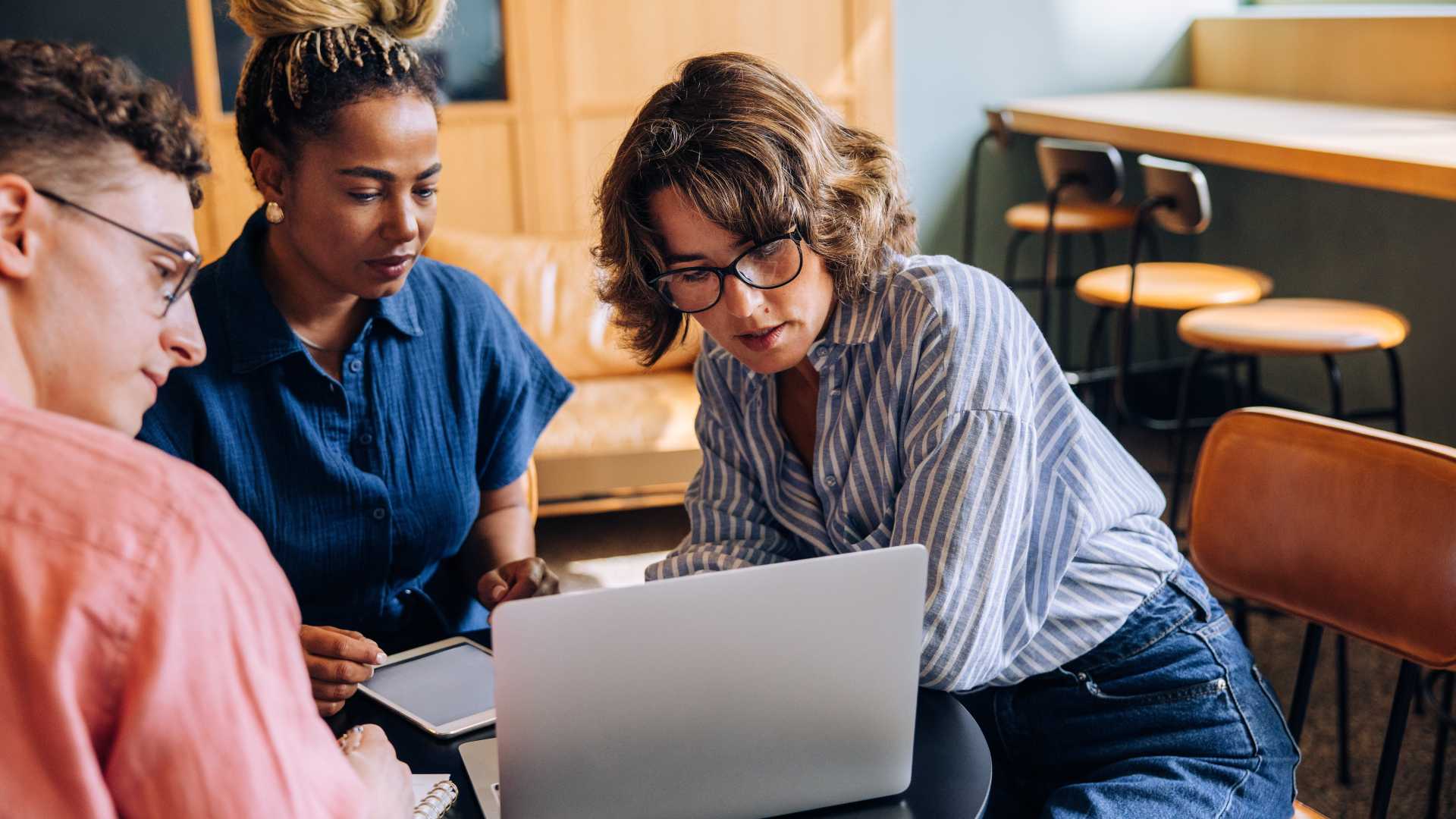 Three cybersecurity professionals collaborate around a laptop during a team training session, illustrating cybersecurity workforce development, hands-on learning and practical skill building.