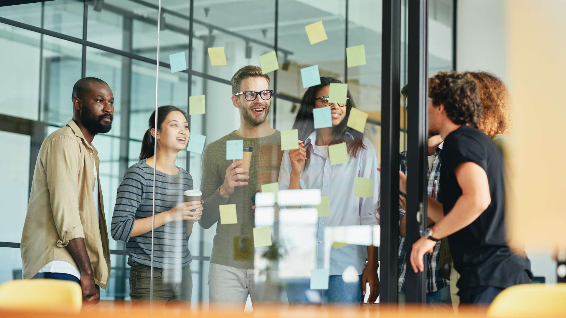 A team collaborates around a glass wall covered with colorful sticky notes. 