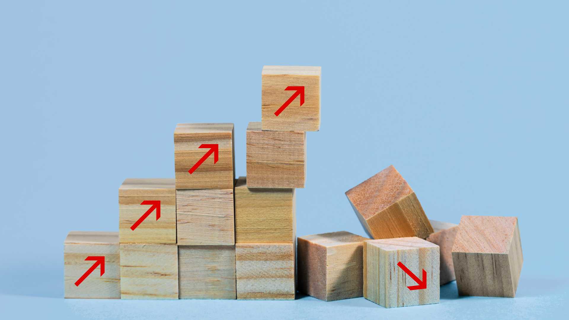 Wooden blocks with upward arrows forming a stable structure beside fallen blocks, illustrating how strong quality systems support consistent training performance and organizational resilience.