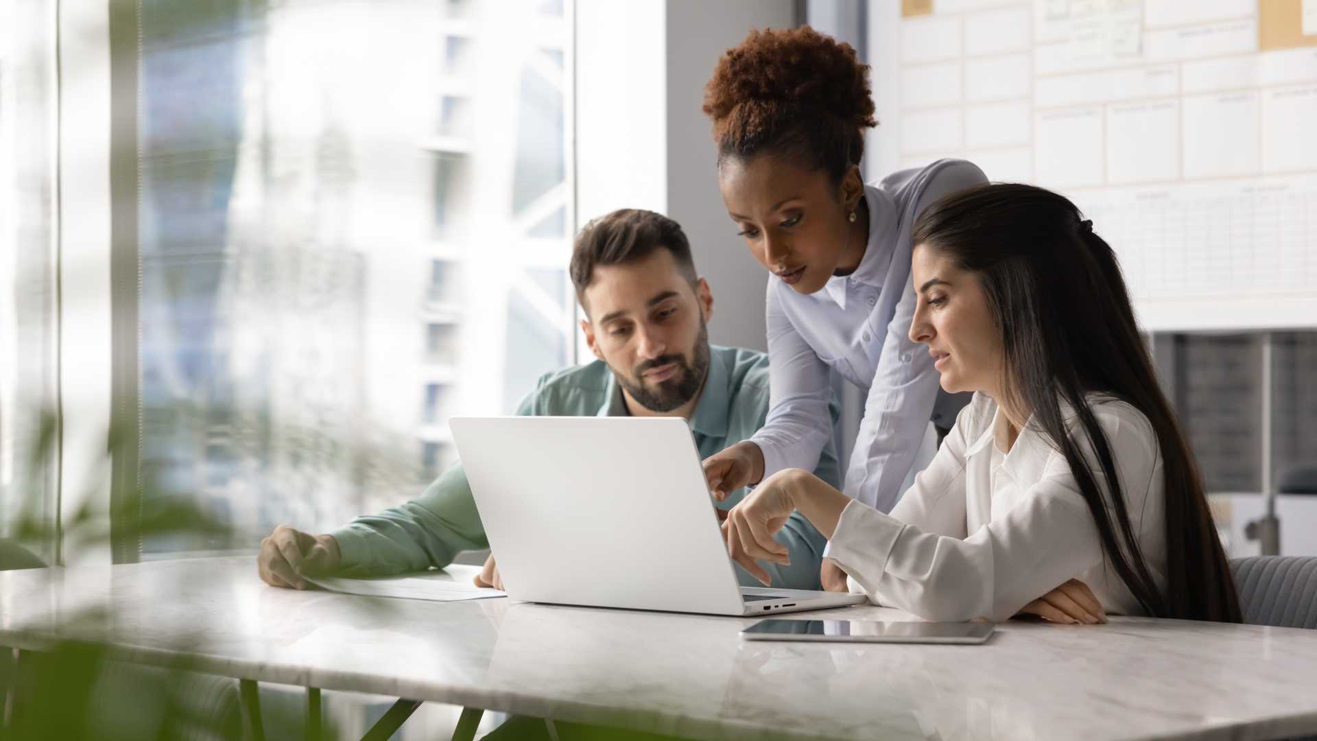 Three colleagues collaborating around a laptop, illustrating leadership development through coaching, feedback and the workplace application of new skills.