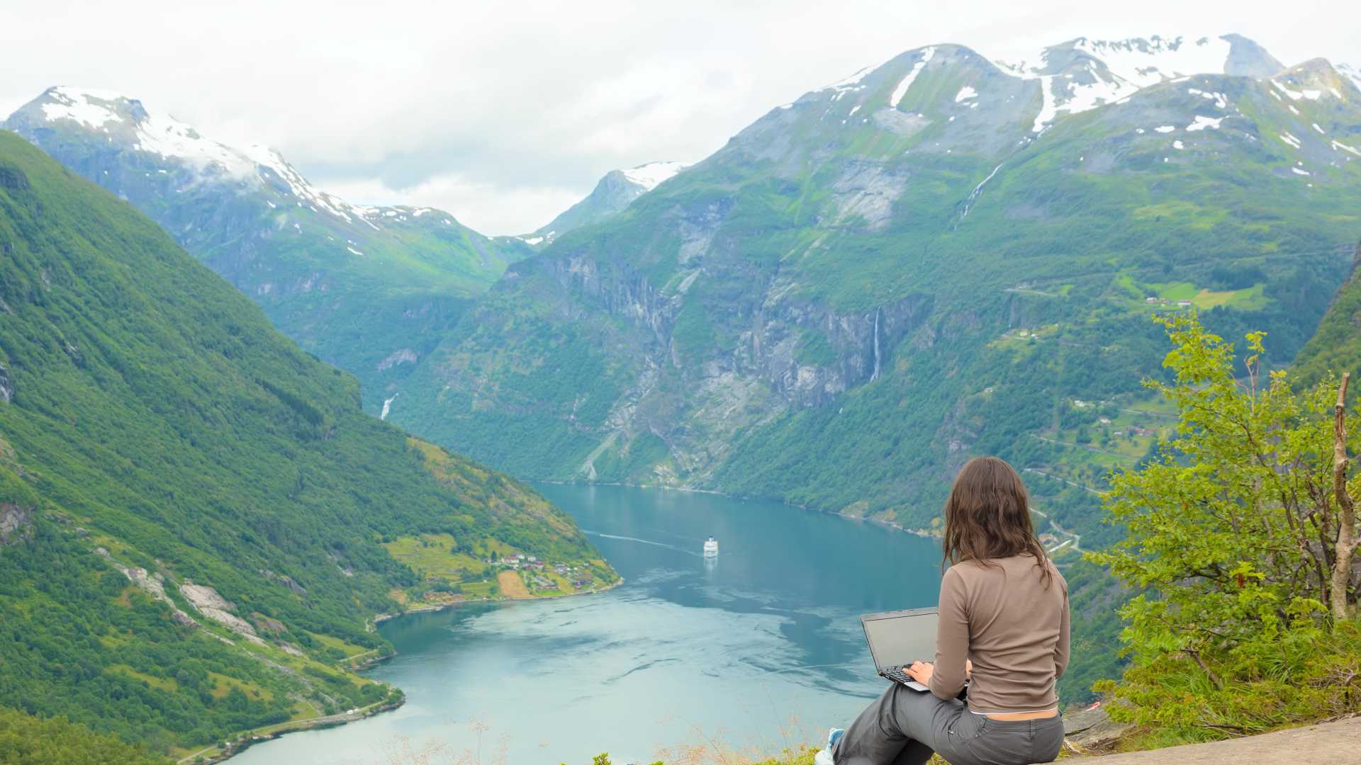 Professional using a laptop overlooking a mountain fjord, illustrating Tripadvisor’s exploration-themed approach to personalized leadership development and professional growth.