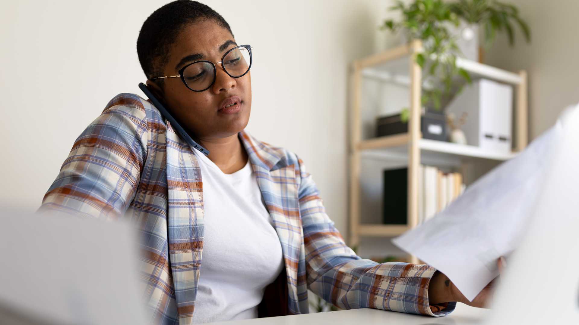 Solo L&D professional multitasking with a phone and paperwork, illustrating the challenge of managing competing tasks, deadlines and responsibilities as a team of one.