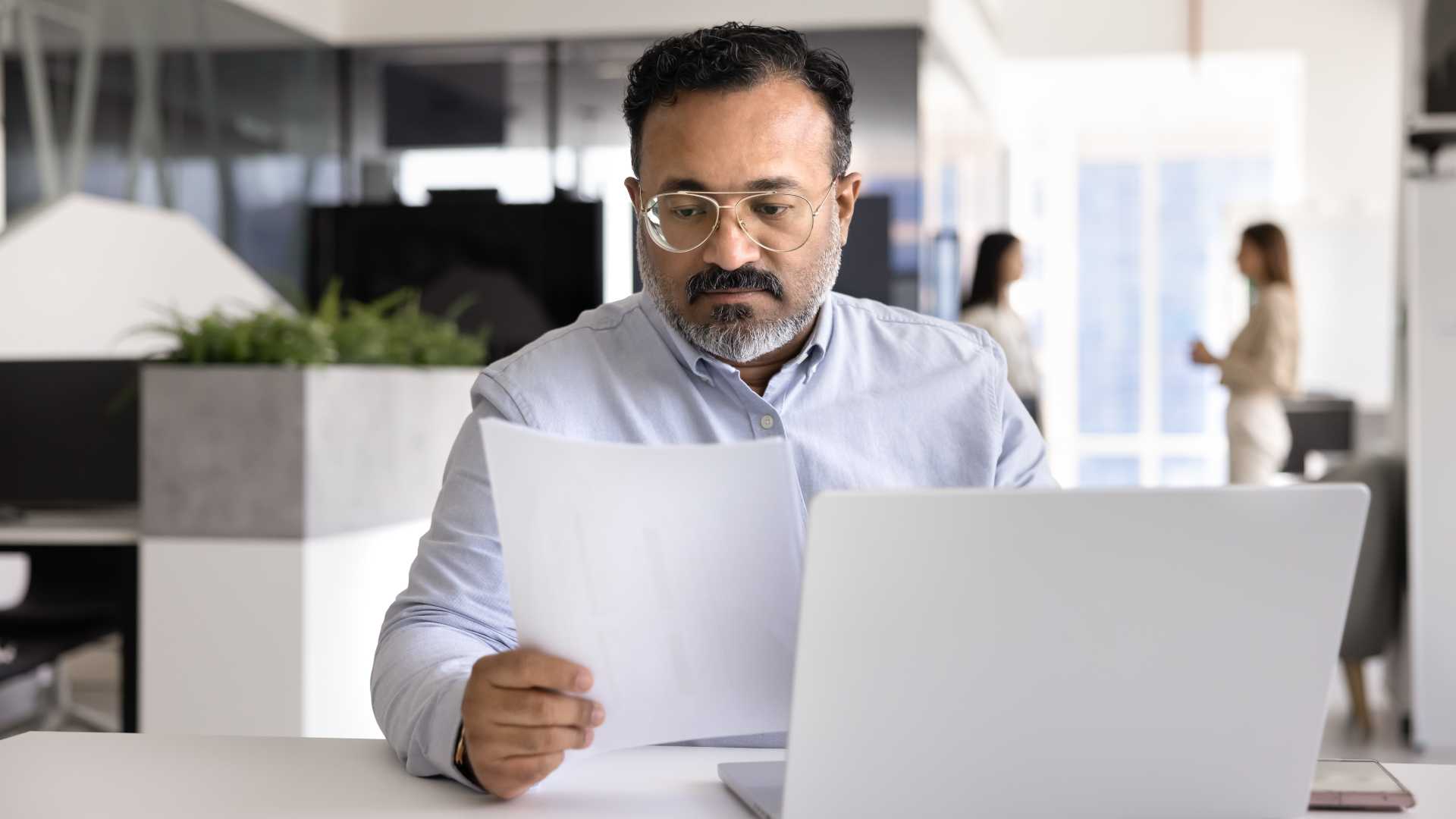 Employee reviewing documents alongside a laptop in an office, illustrating workplace compliance, responsible AI use and ethical decision-making guided by organizational policies.