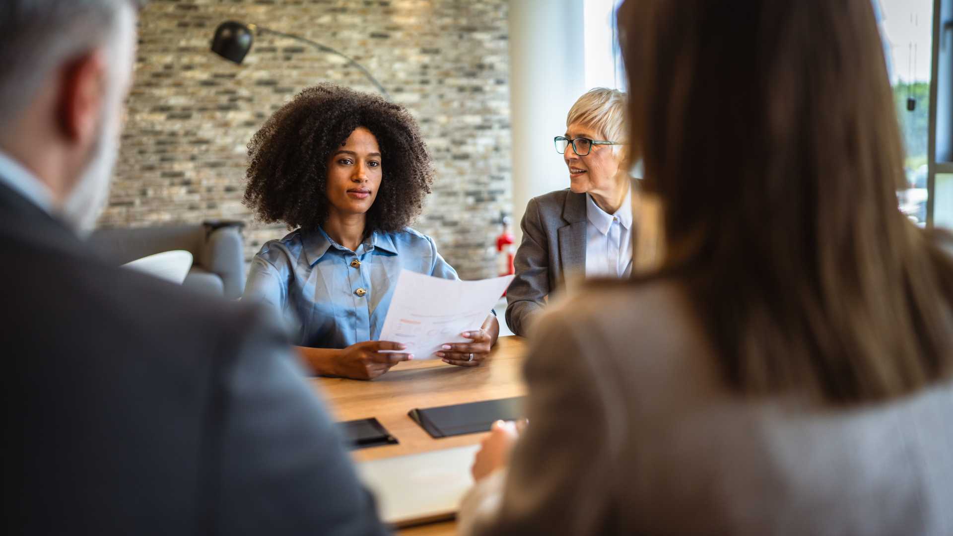 L&D professional reviewing documents with colleagues during a business meeting, illustrating organizational buy-in for professional certifications, career development and strategic investment in skills.