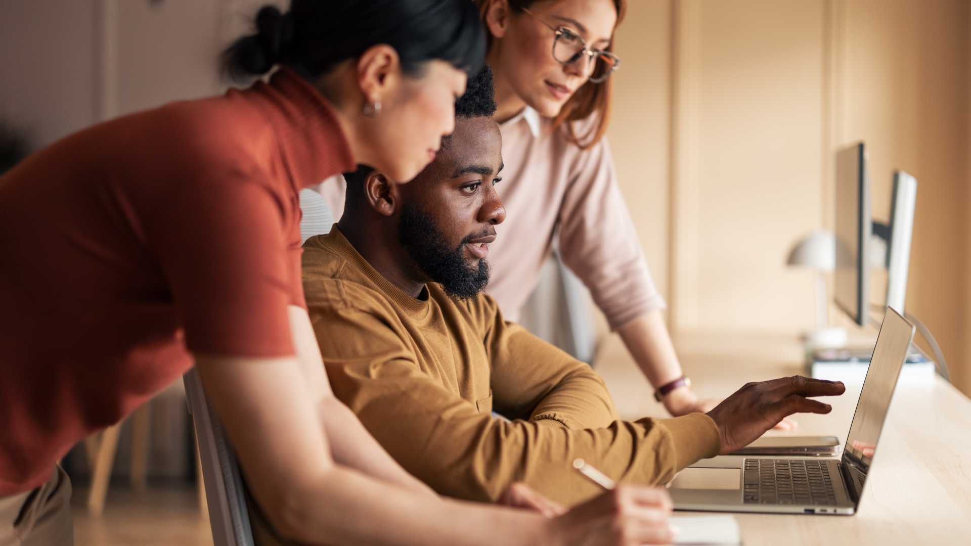 Three professionals collaborating around a laptop, illustrating how AI-enabled coaching tools can support employee development, knowledge sharing and human-centered learning.
