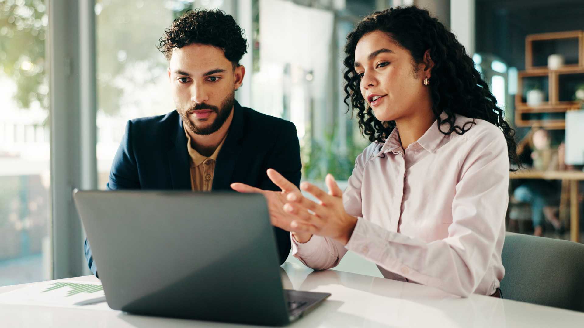 Two professionals reviewing information on a laptop, illustrating collaborative performance coaching, workplace training evaluation and the use of real-world data to improve employee skills.