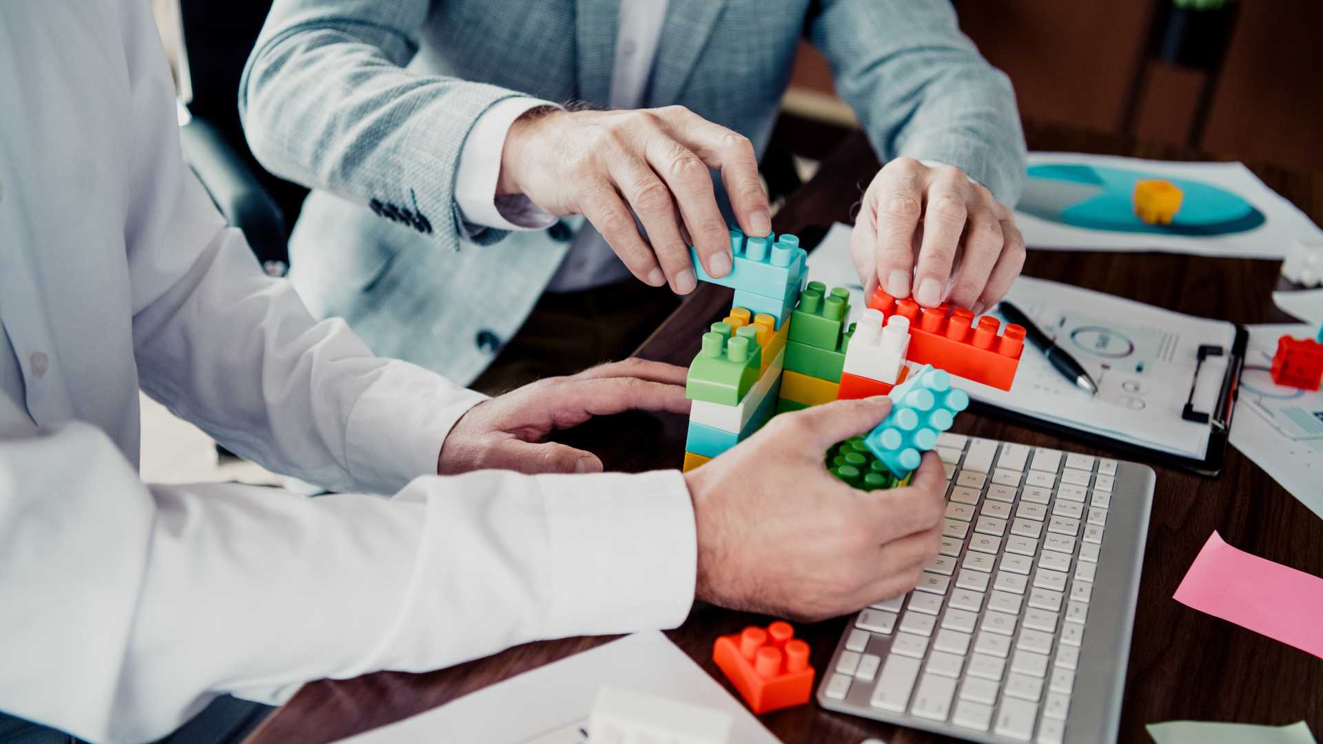 Professionals assembling colorful building blocks together, illustrating training synthesis through the integration of multiple skills, collaborative problem-solving and practical application of knowledge.