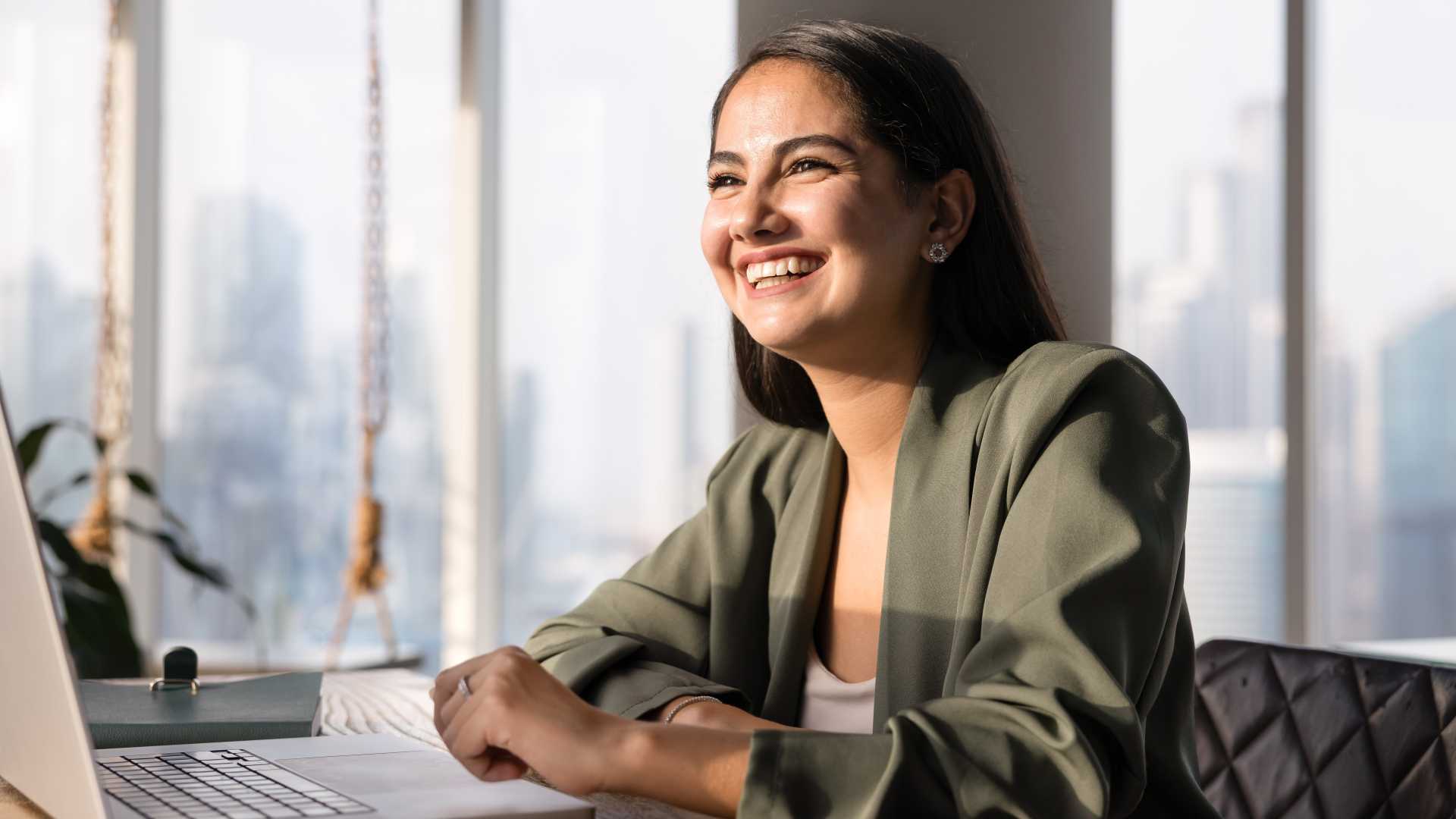 Smiling professional seated at a laptop in a modern office, illustrating employee confidence, workplace competence and the application of professional skills.