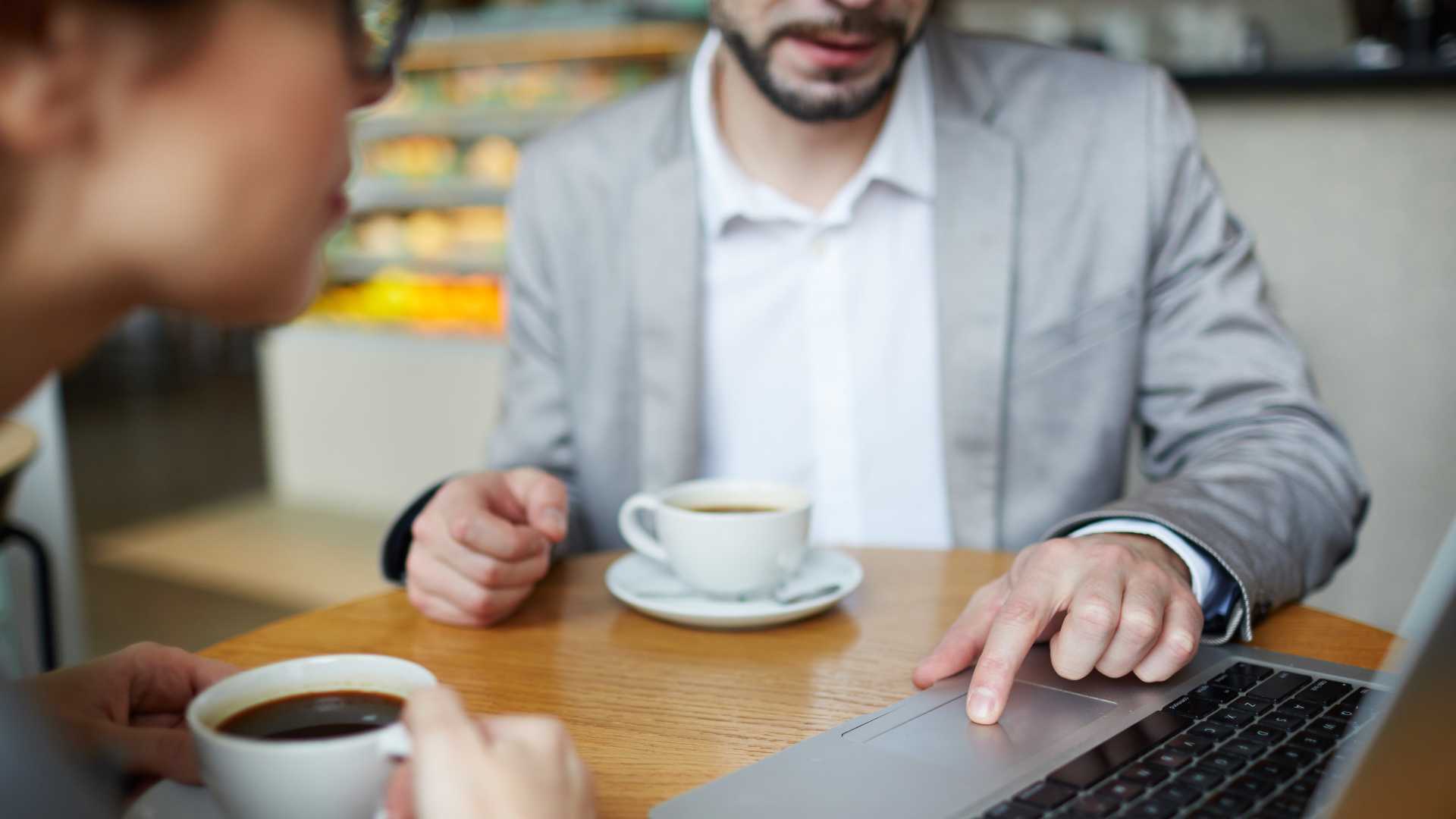 Manager and employee reviewing information on a laptop during a one-on-one conversation, illustrating performance feedback, coaching and employee development.